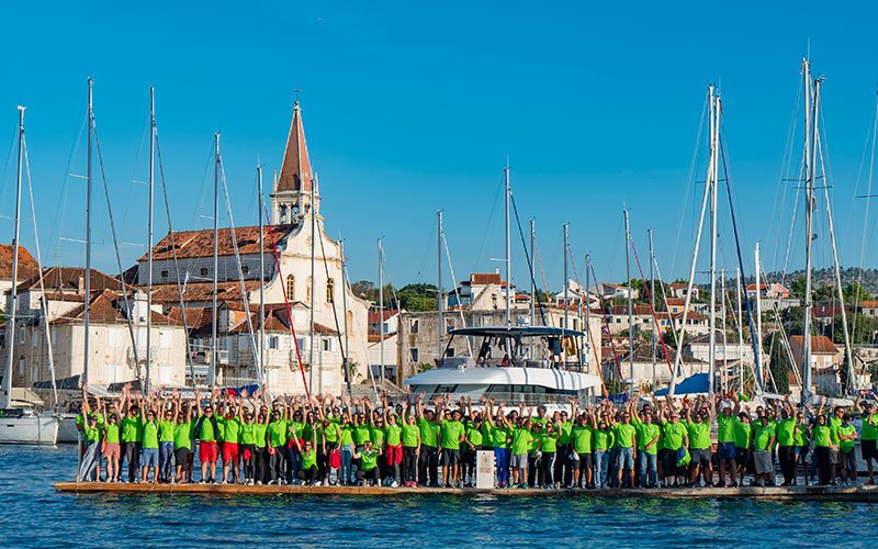 Many people together, near the sea, wearing green t- shirts of Green Sail and waving their hands
